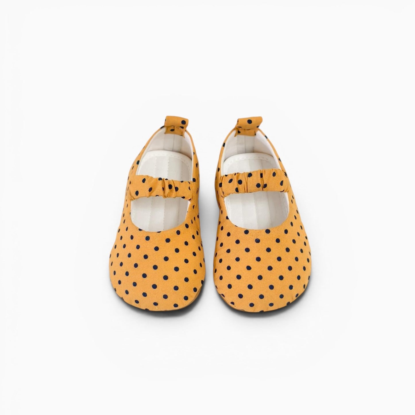 A pair of toddler Mary Jane shoes in mustard yellow with black polka dots, shown from a top-down view on a white background.